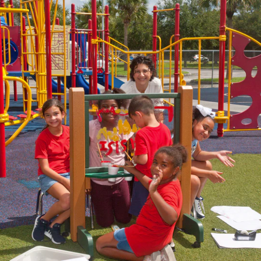 Children painting on a clear double-sided recycled plastic art easel outdoors at a colorful playground