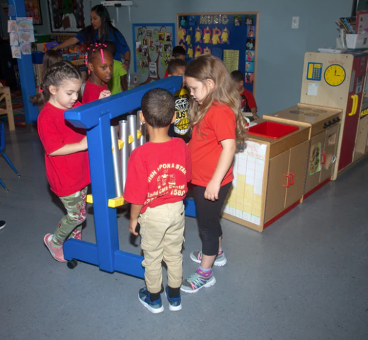 Children playing indoors with a blue 6-note musical chime unit featuring aluminum tubes and a recycled plastic frame