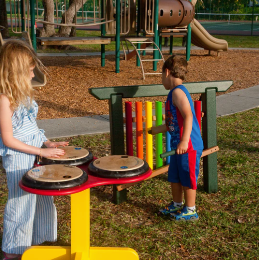 Children playing on colorful outdoor musical instruments including rainbow chimes and drum pads at a playground