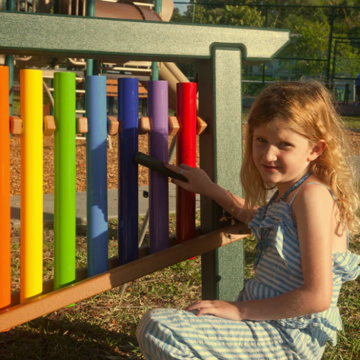 Child playing colorful outdoor musical chime bars arranged in rainbow colors for interactive rhythm play