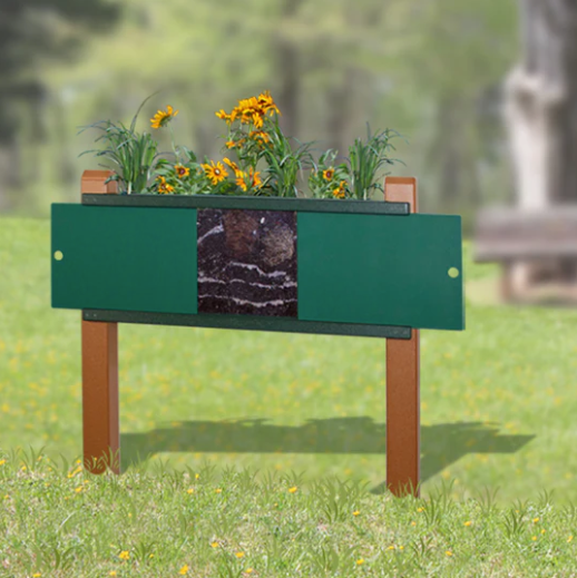 Elevated green planter with front soil viewing window, yellow flowers, wooden legs, on grass outdoors