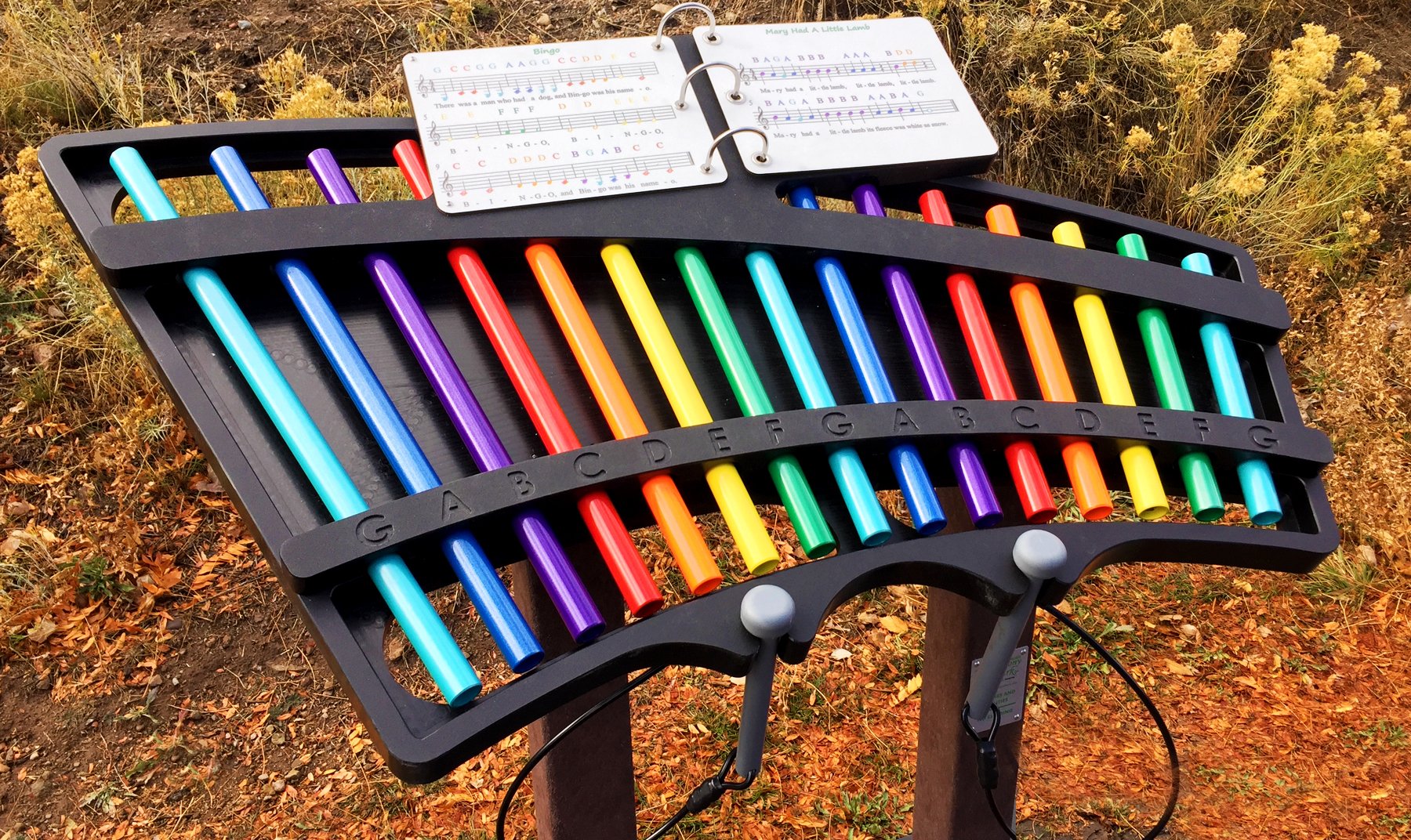 Serenade Outdoor Musical Park Instrument with 15 colorful diatonic chimes, mallets, and songbook in natural play area setting