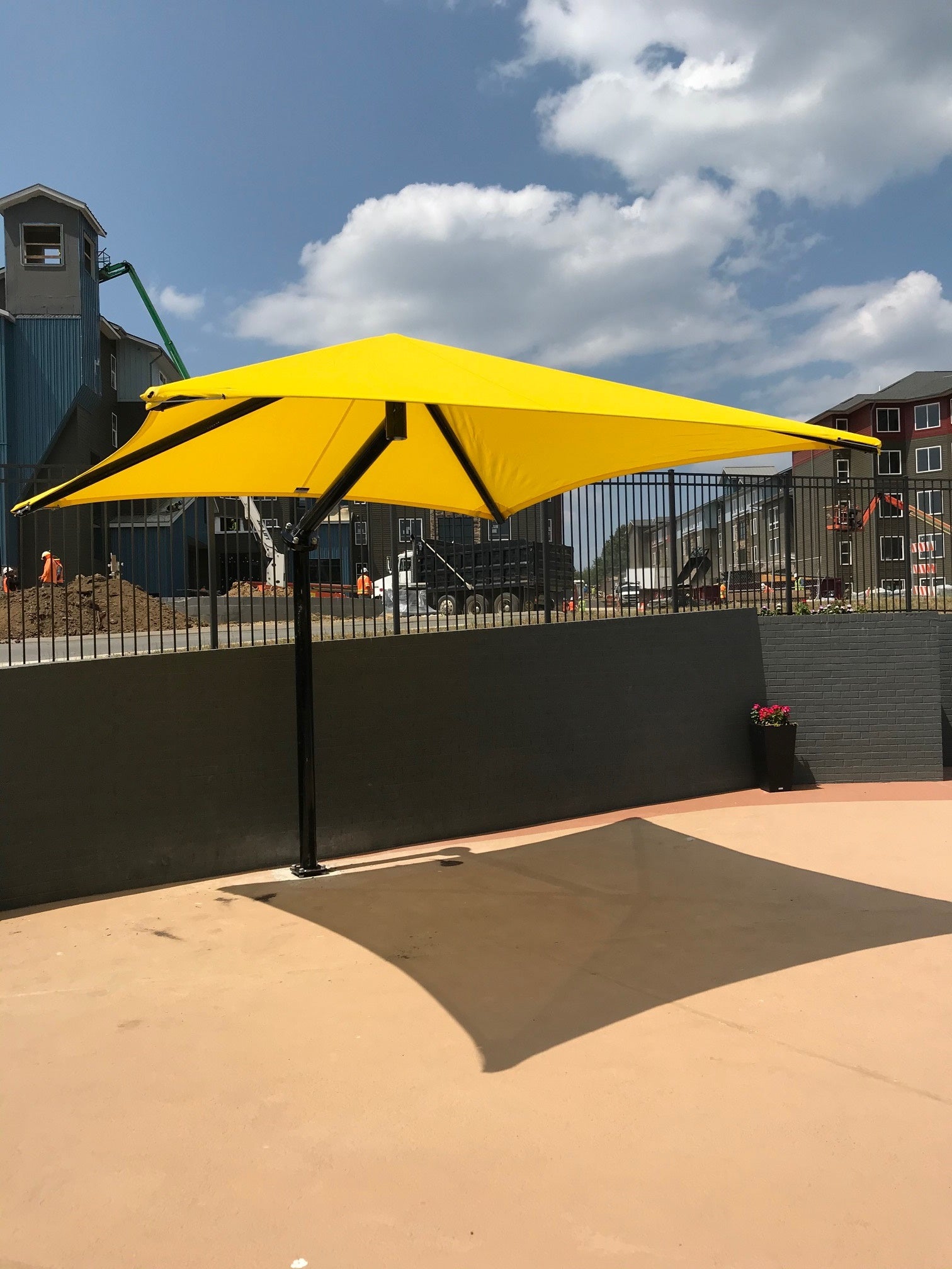 Bright yellow single post cantilever shade with pyramid canopy casting shadow on paved outdoor surface