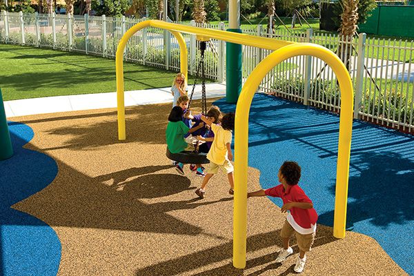 Yellow arch tire swing with children playing on blue and brown safety surfacing in a fenced playground area