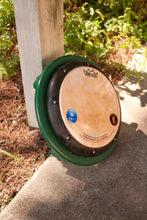 Green circular outdoor drum table with natural tunable drum-head, surrounded by sunlight and foliage