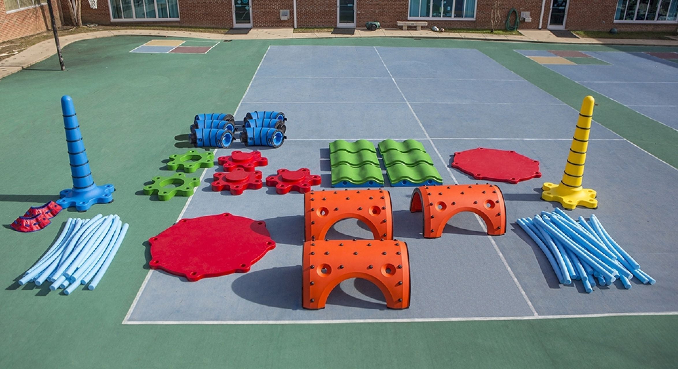 Colorful modular outdoor play equipment with tunnels, cones, platforms, and rods arranged on playground surface for interactive play and learning