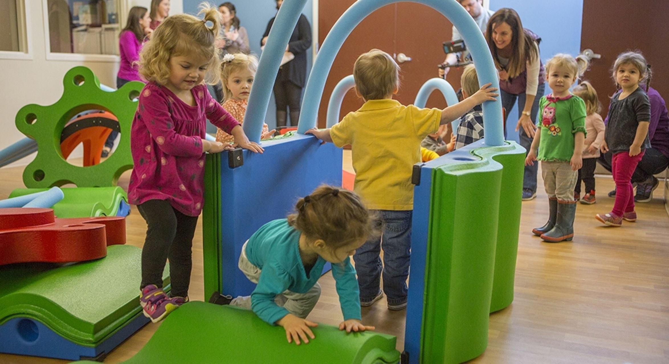 Children playing on colorful indoor interactive play equipment featuring waves, bumps, and noodle-shaped elements