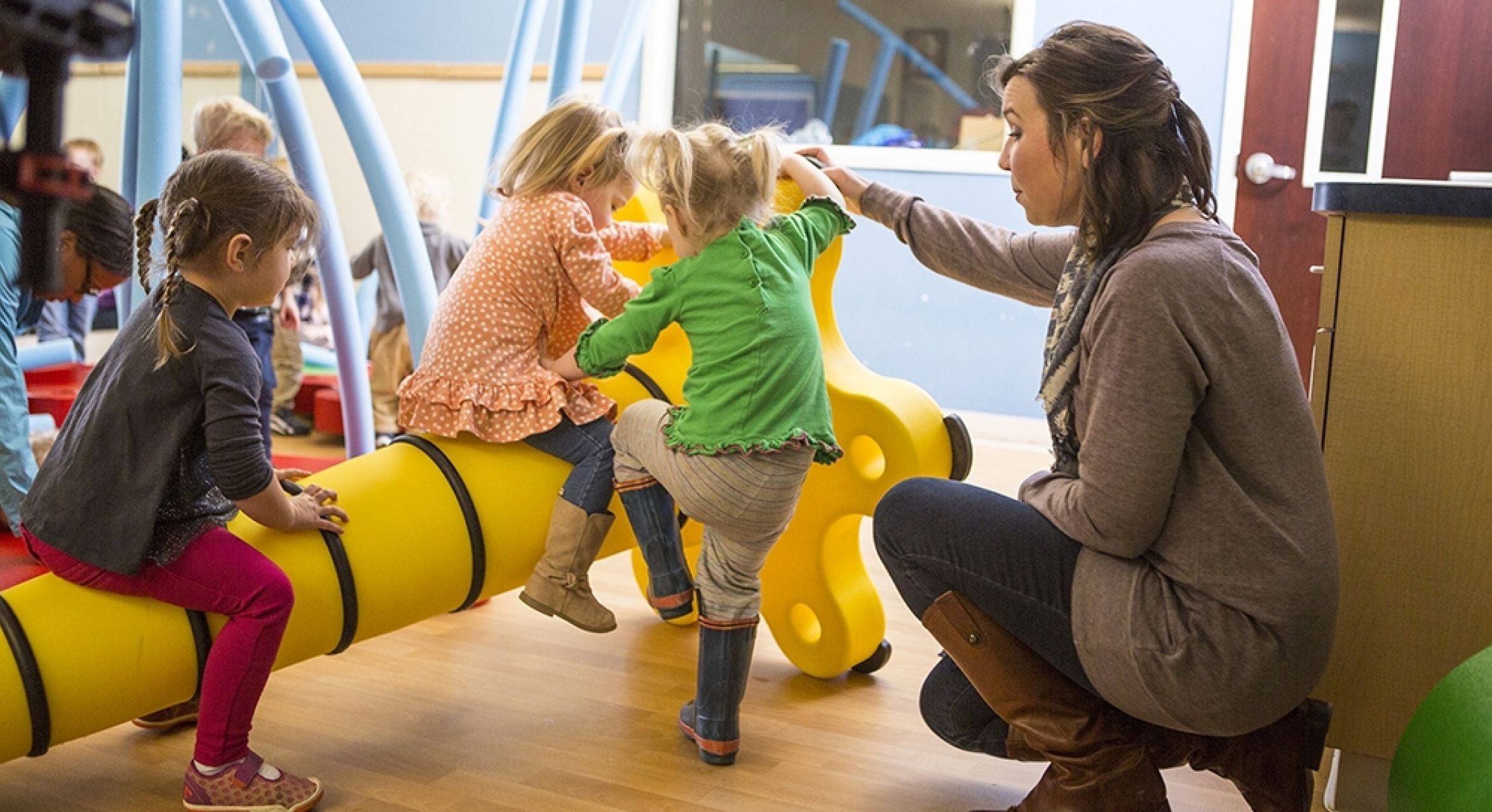 Children playing on bright yellow interactive indoor play equipment with adult supervision in a learning environment
