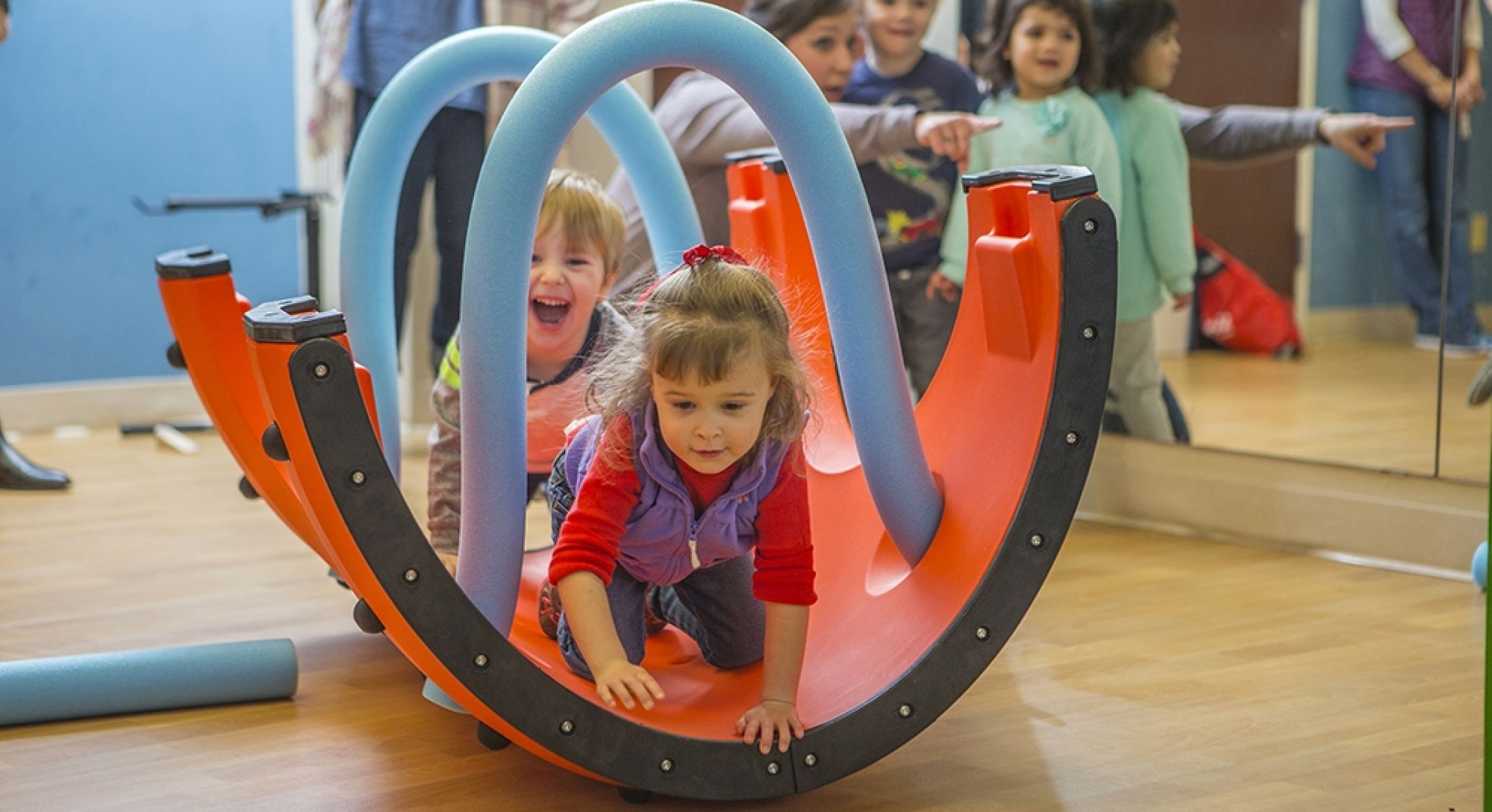 Children playing with colorful curved orange panels and blue foam arches in an interactive indoor play setting