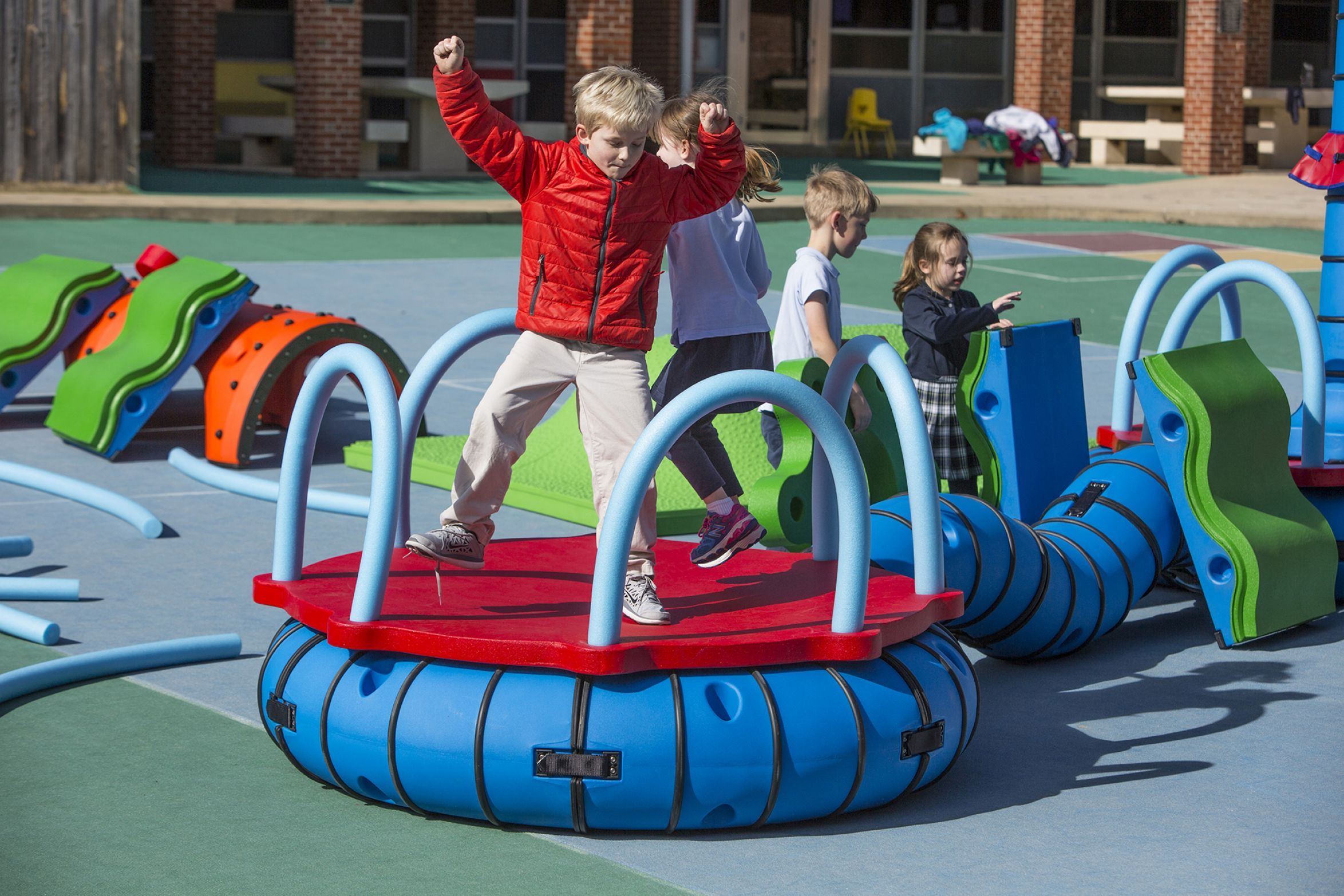 Children engaging with colorful interactive playground equipment featuring blue loop rings and green climbing elements.
