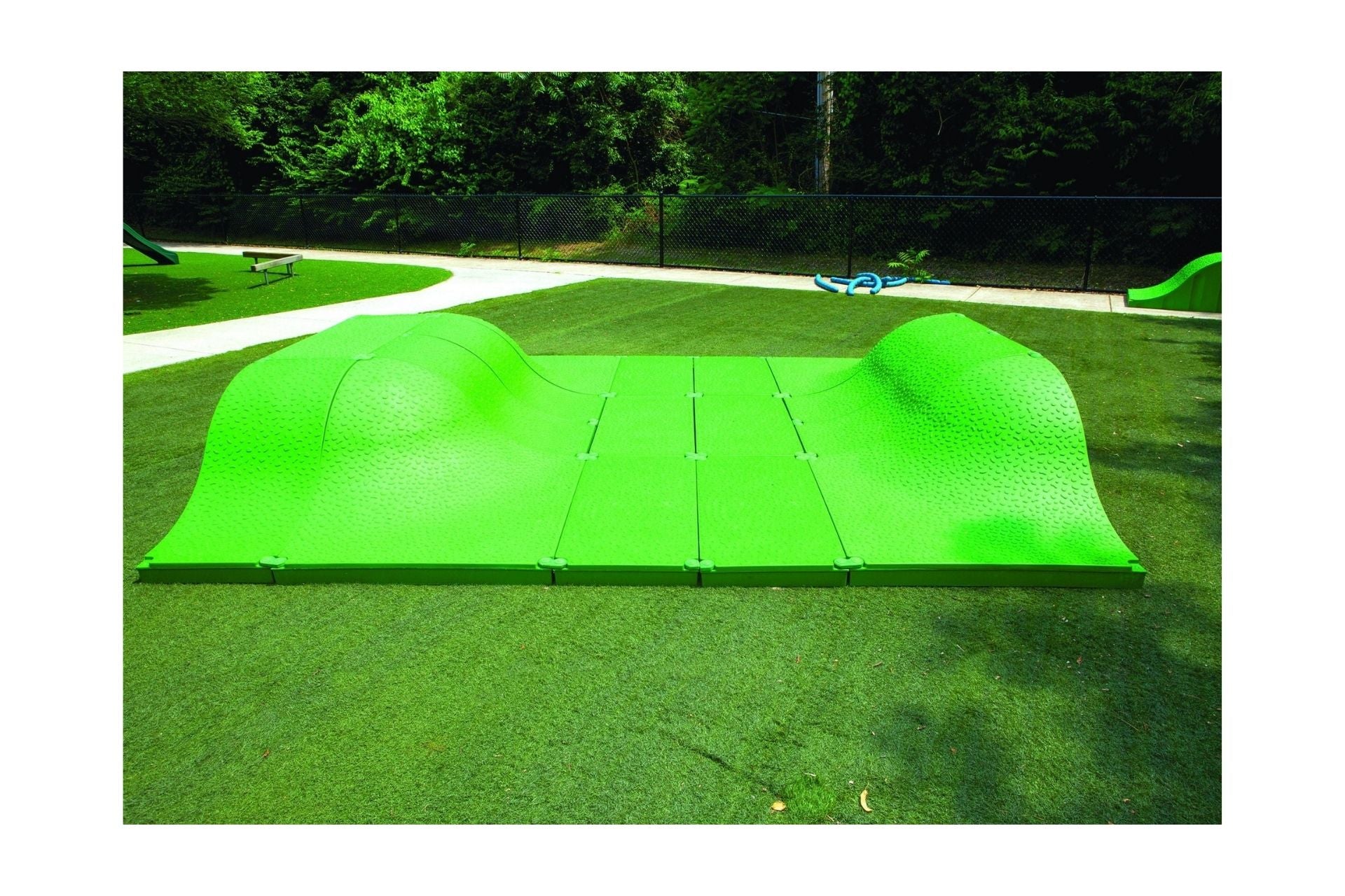 Bright green modular play mound with smooth and textured curved surfaces on artificial grass in an outdoor playground setting