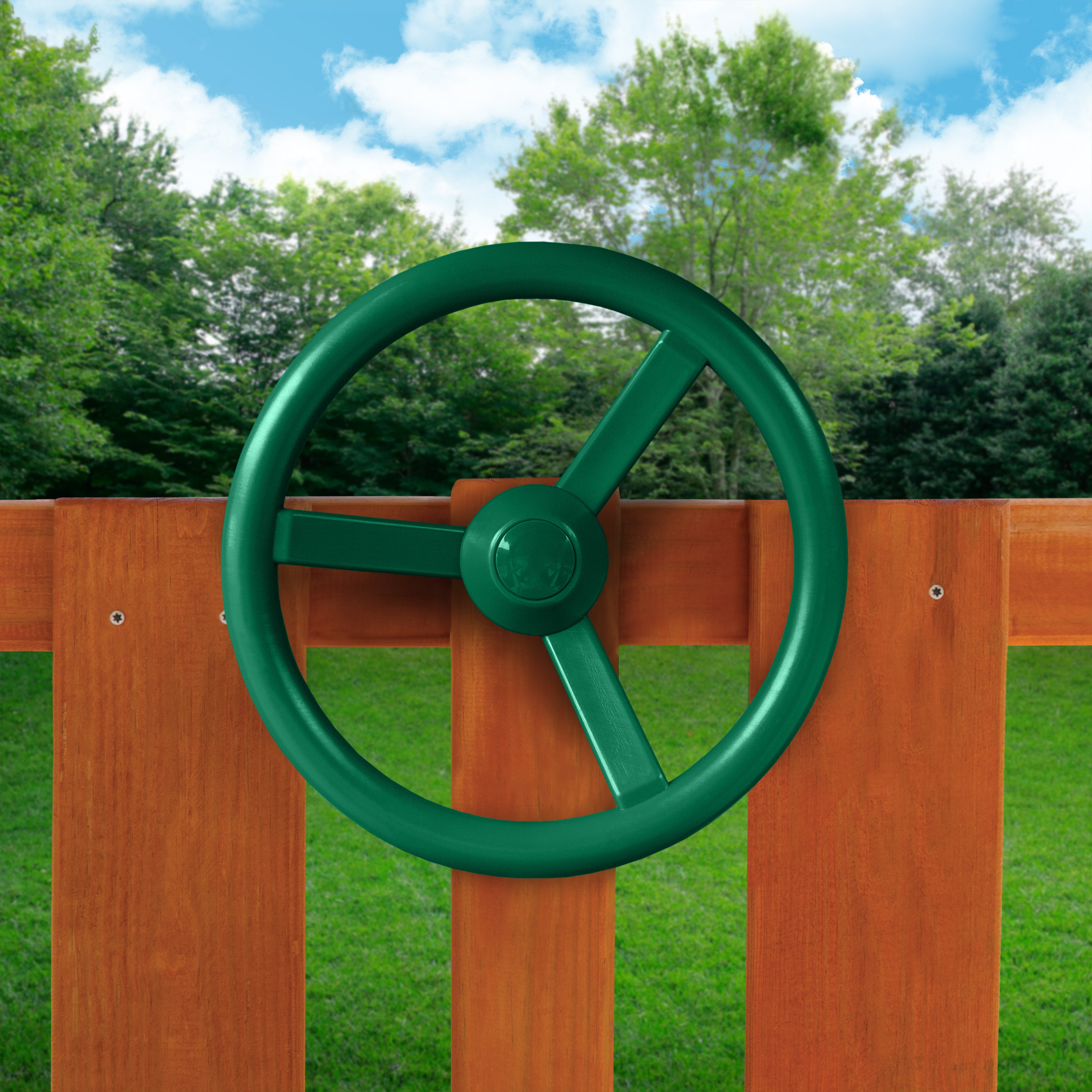 Green Steering Wheel Swing Set Accessory mounted on wooden playset railing with outdoor grass and trees background