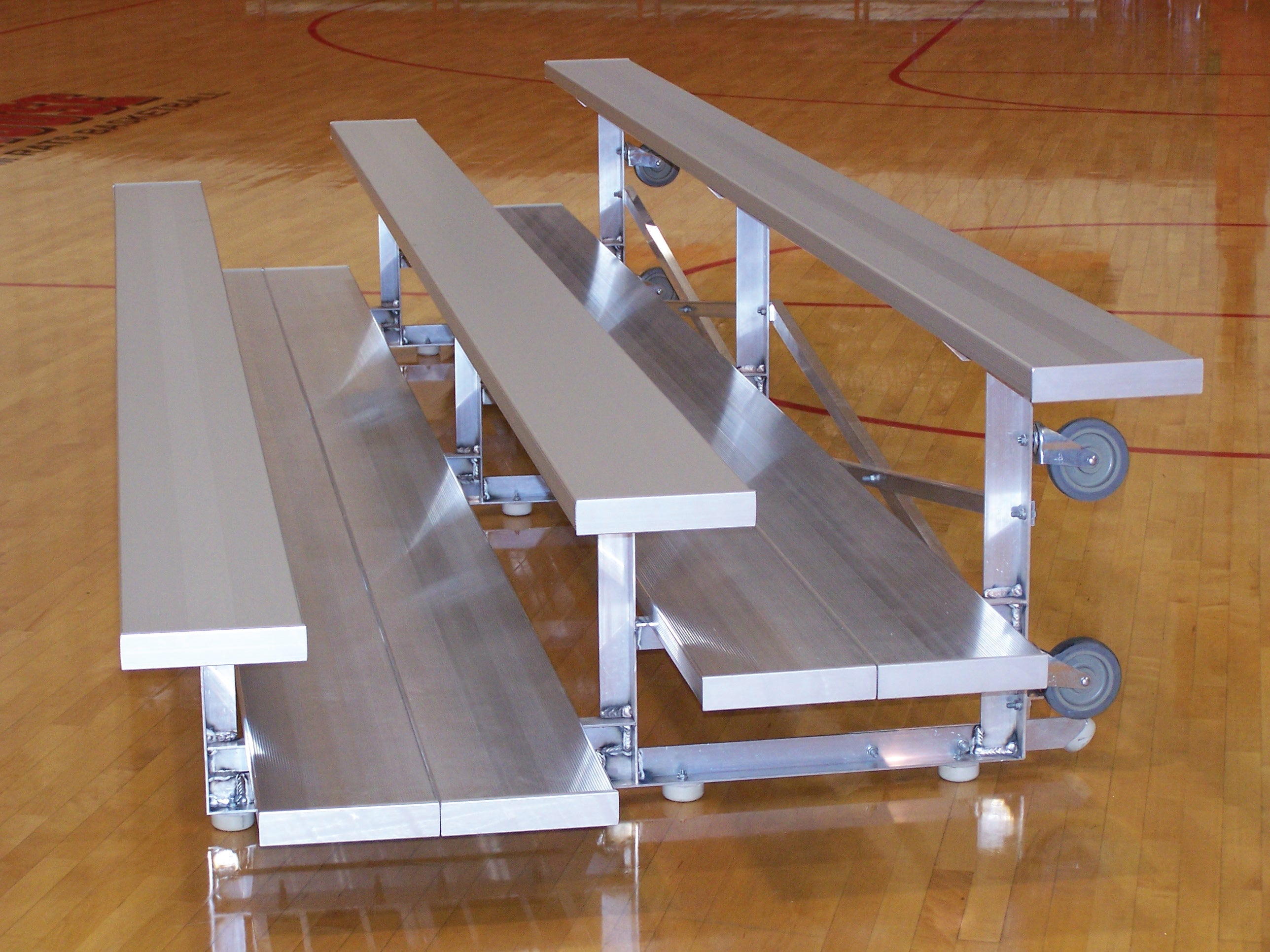 Aluminum 3-row portable bleachers with casters on polished gym floor for flexible indoor seating