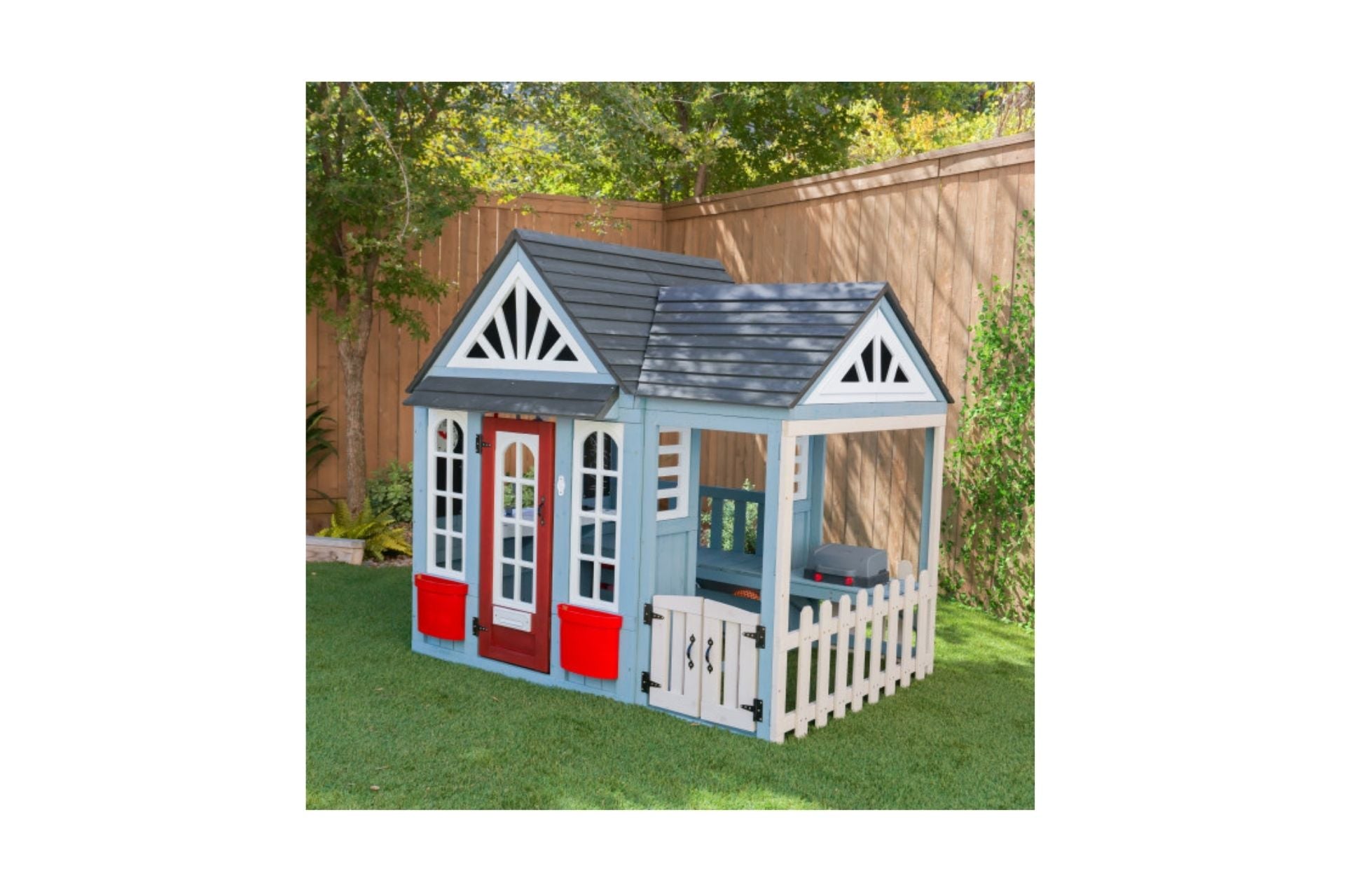 Timber Trail Wooden Outdoor Playhouse with blue walls, red door, white picket fence, planter boxes, and outdoor grill on green lawn