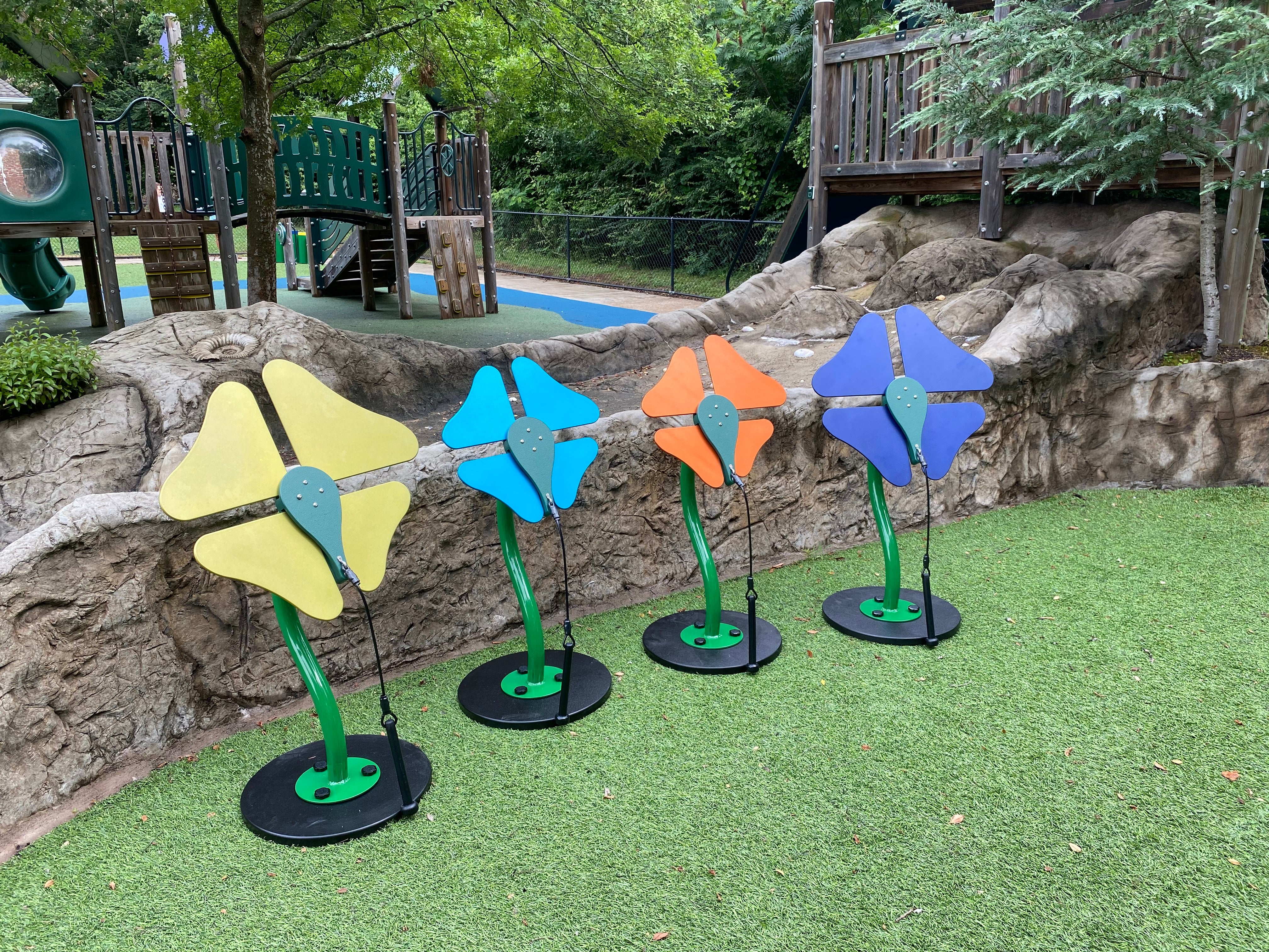 Colorful flower-shaped outdoor musical instruments with attached mallets on artificial grass near playground equipment