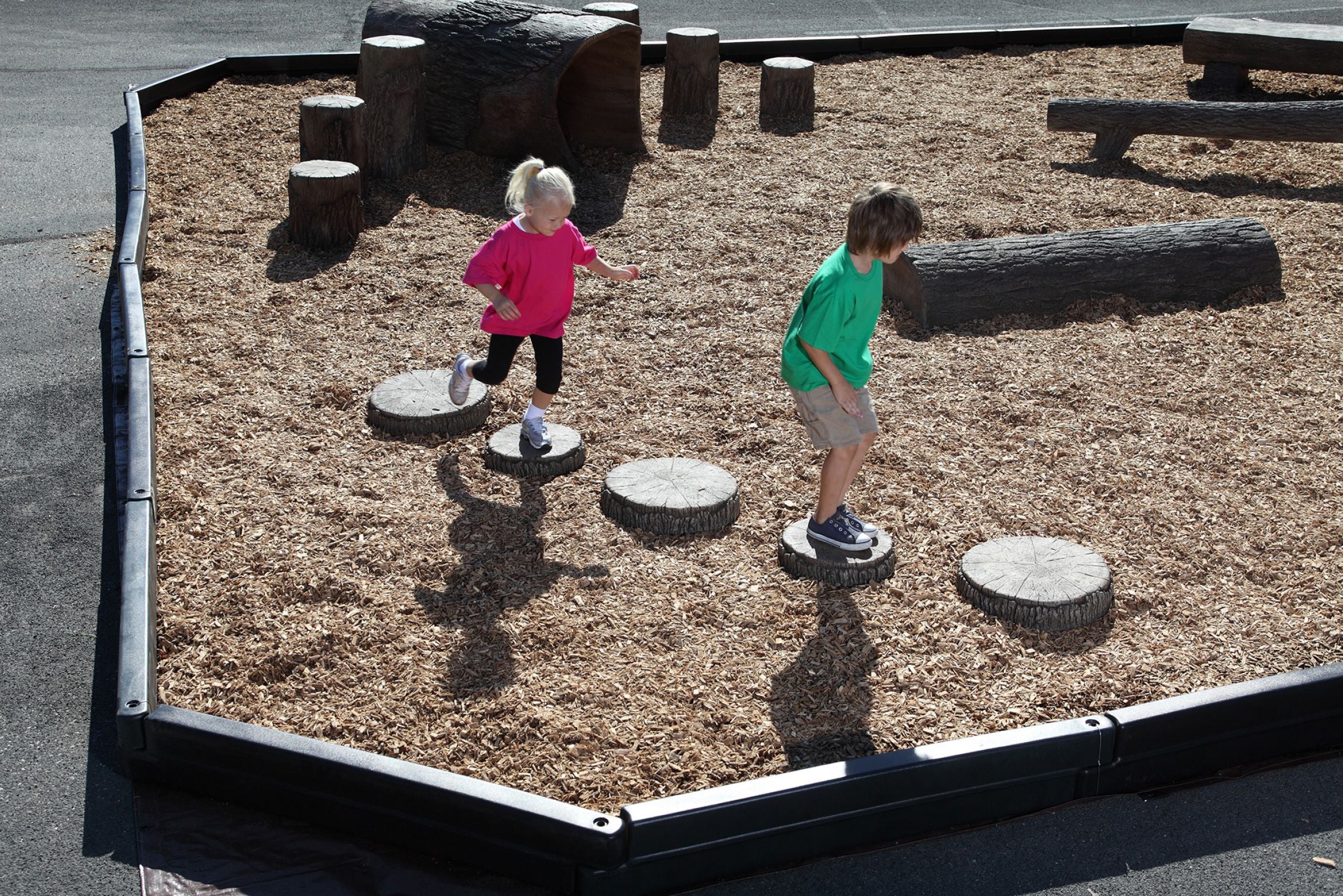 Children playing on nature-themed tree slice steppers in an outdoor playground setting.