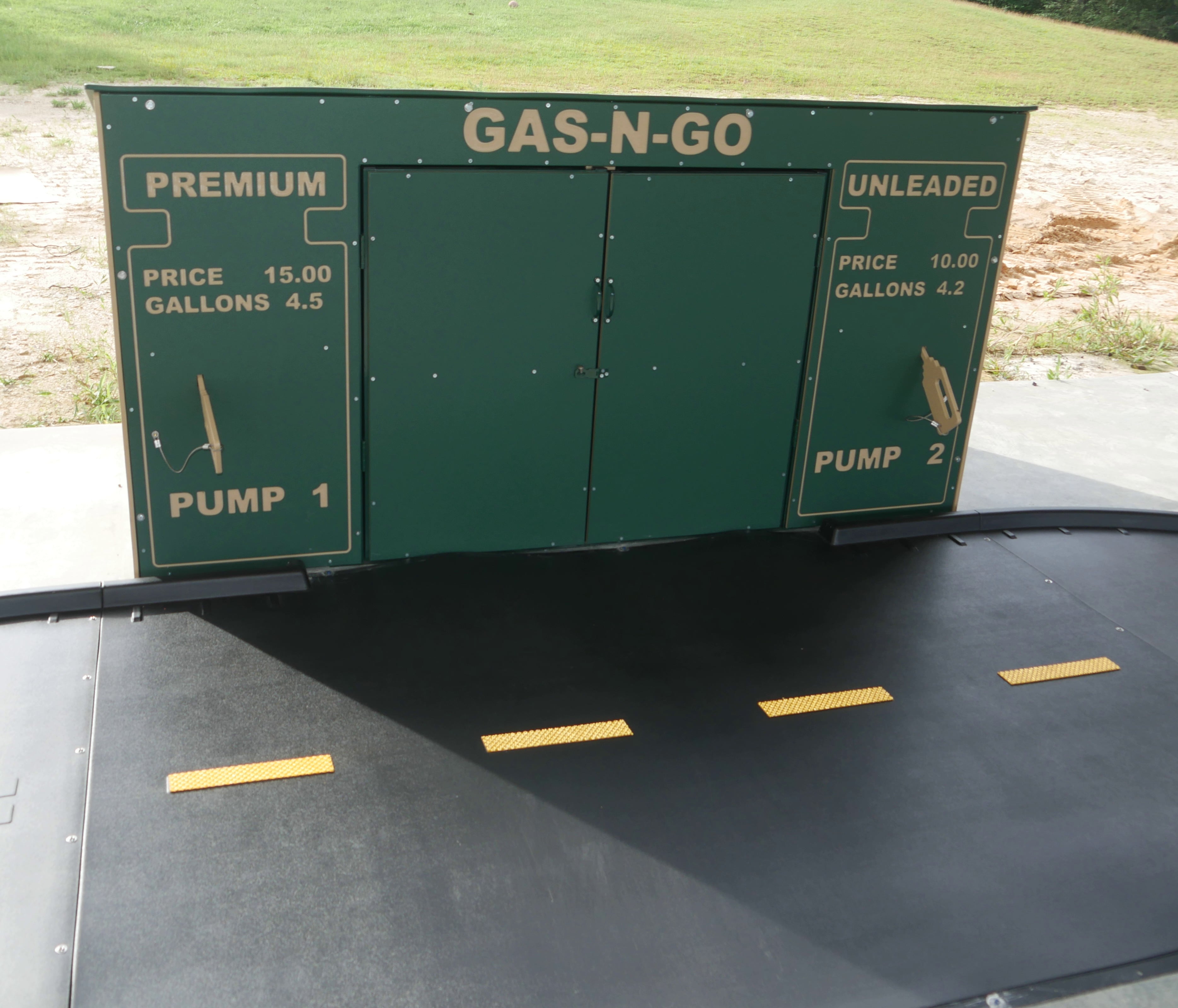 Outdoor green play structure resembling a gas station with two pump panels and a black play surface featuring yellow road markings