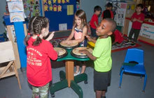 Three children playing on a colorful indoor triple drum table with three drum pads designed for interactive rhythm play