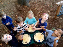 Three children playing on an outdoor triple drum table with varied drum pads for interactive rhythm play