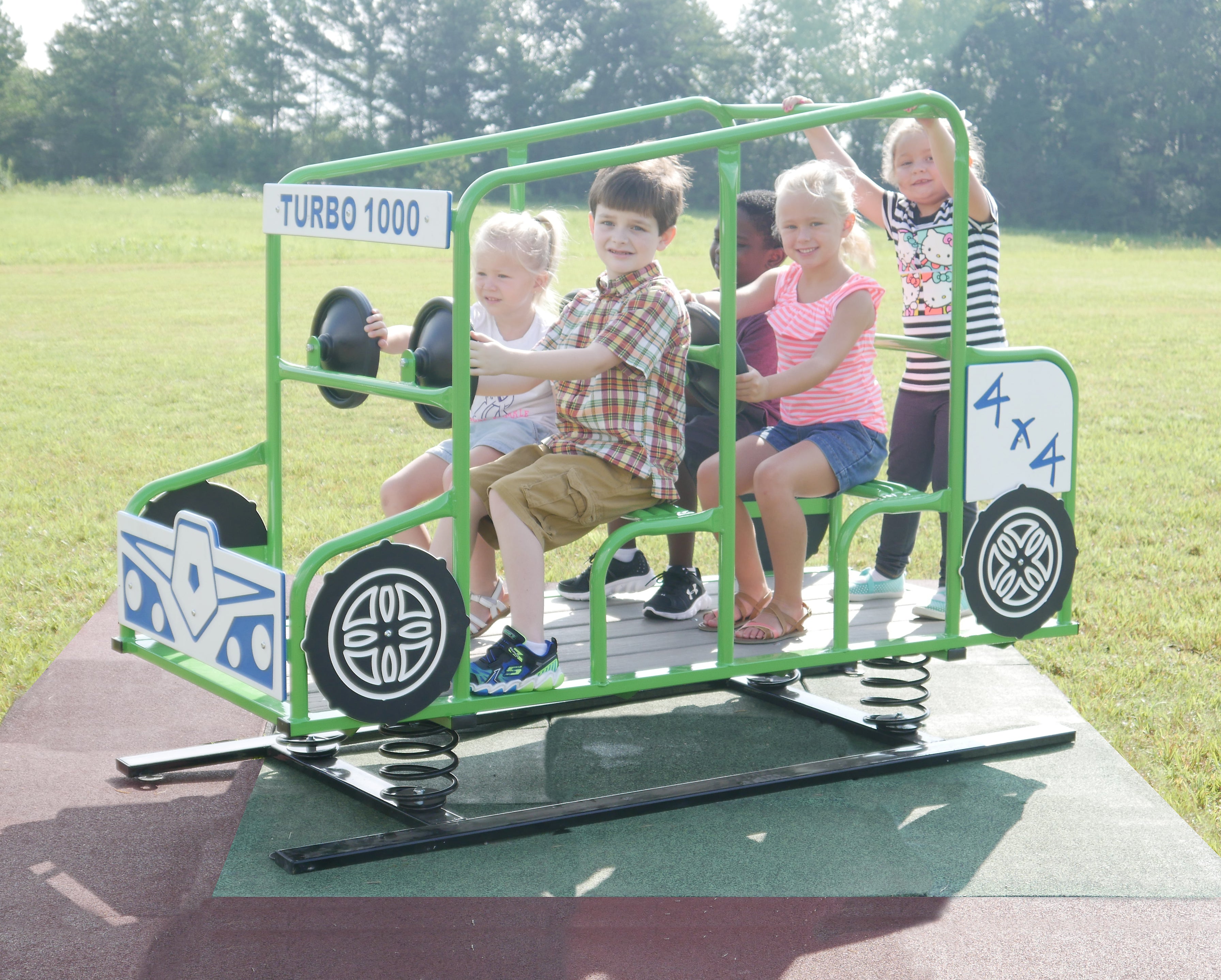 Green multi-passenger spring rider shaped like a vehicle with steering wheels and children playing outdoors on playground equipment