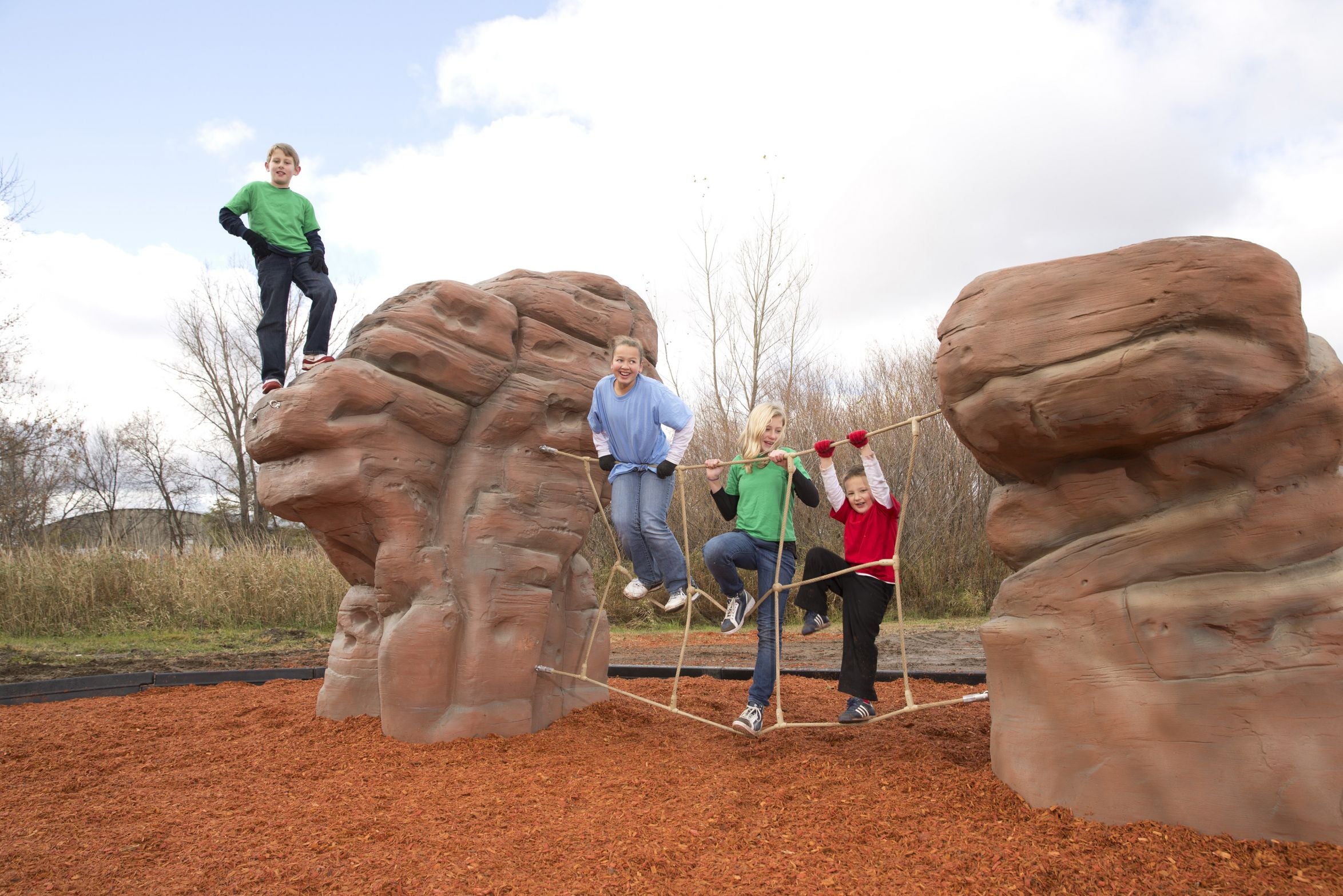 Nature Rocks Sierra Nevada Climbing Rock with children climbing sandstone boulders connected by a cargo climber net outdoors