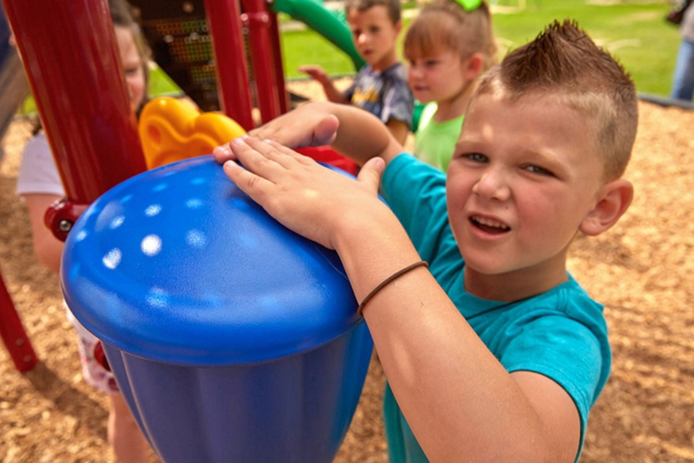 Child playing a blue outdoor playground drum near slides, monkey bars, and climbing structures in a park setting