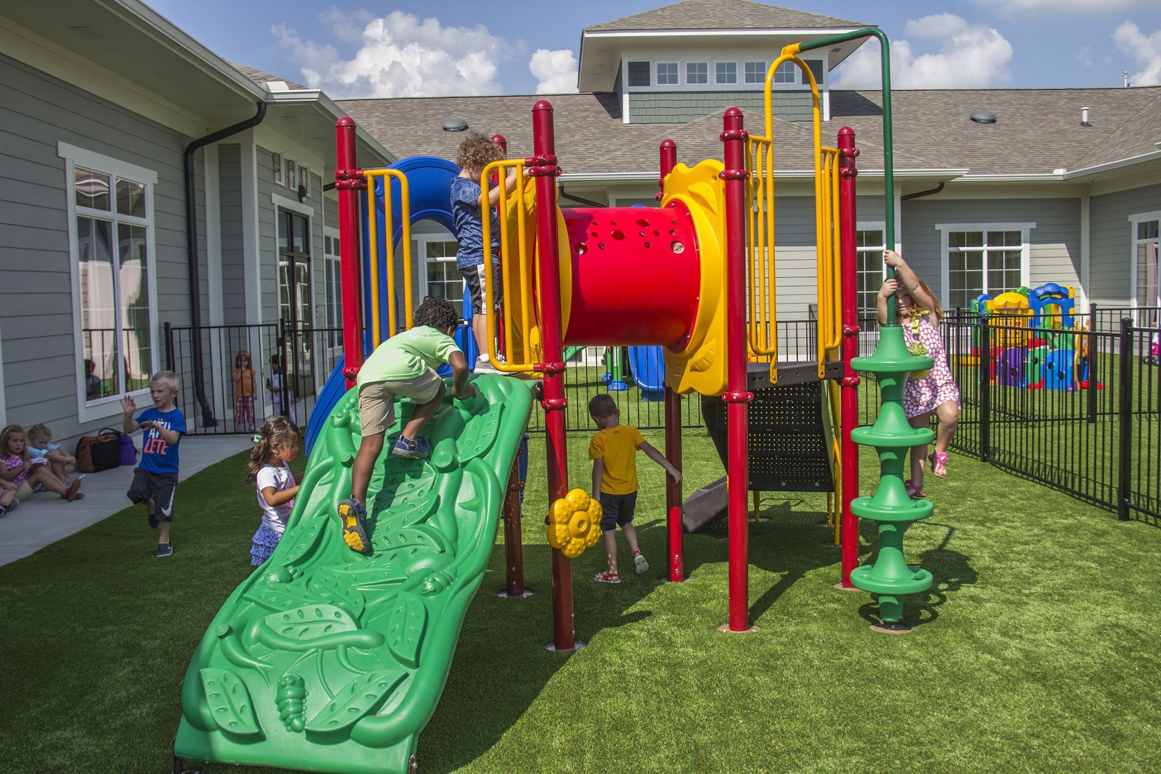 Compact colorful playground with slide, climbing wall, tunnel, spinning pole, and children playing on artificial turf
