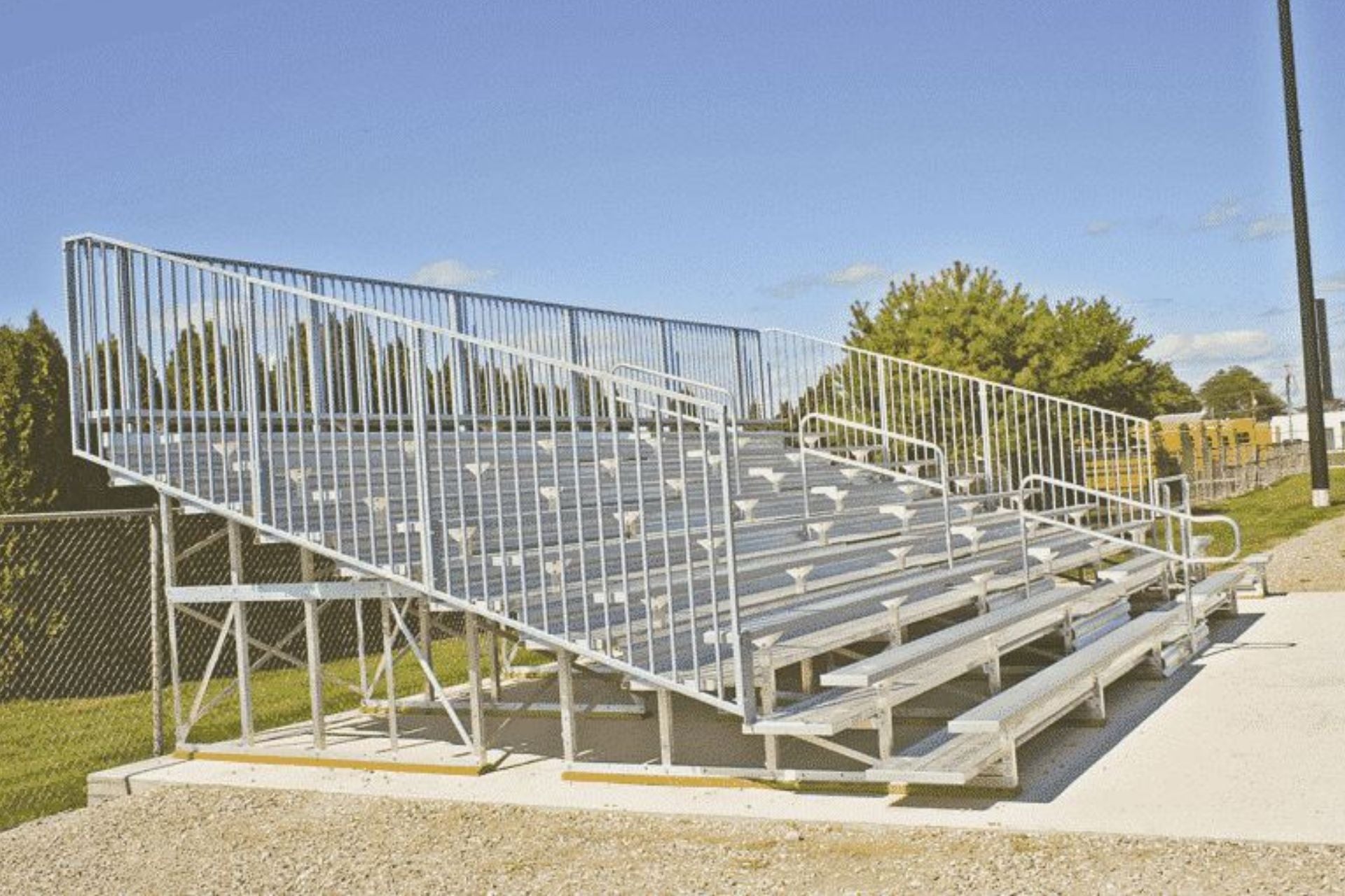 Aluminum five-row outdoor bleachers with vertical picket guardrails, handrails, and multiple seating rows on concrete base