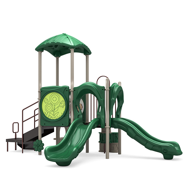 Green and beige playground structure with two straight slides, leaf-shaped roof, flower panels, climbing stairs, and ADA transfer station.