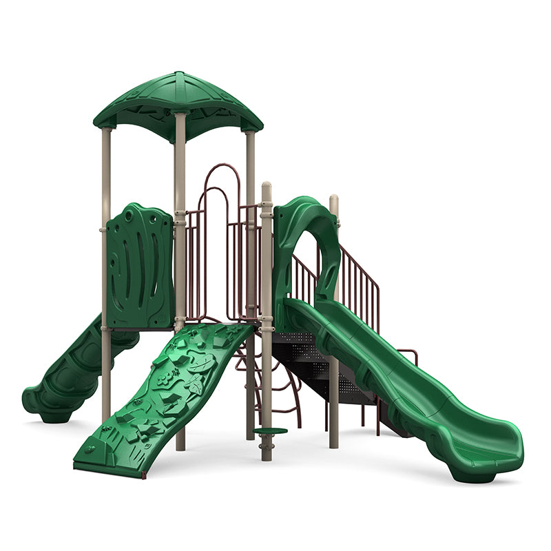 Outdoor playground with neutral leaf-shaped roof, two green slides, rock climbing wall, and arch climber in natural setting
