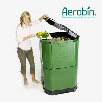 Green insulated compost bin with hinged lid and lower access door, woman adding organic waste for aerobic composting