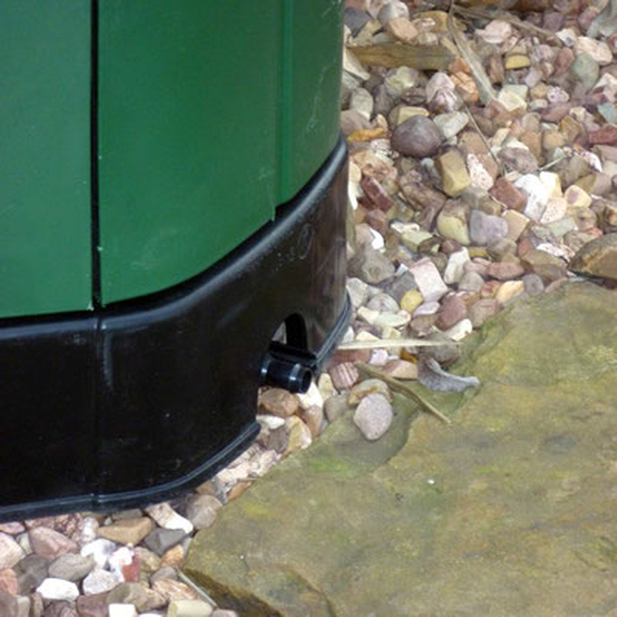 Green insulated compost bin base with black leachate collection spout on gravel and stone surface