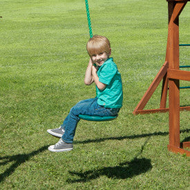 Child sitting on green heavy-duty plastic disc swing with rope, attached to wooden playset outdoors on grass