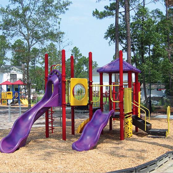 Commercial playground with purple slides, red posts, yellow panels, bridge, canopy, and climbers on mulch in a park setting