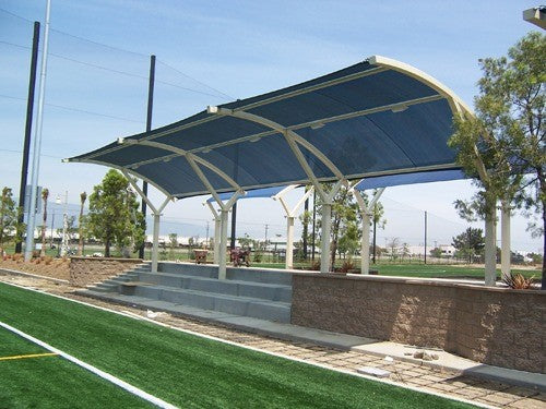 Eclipse 2 Post Arch Shade Structure with curved blue canopy over outdoor seating near sports field and landscaping