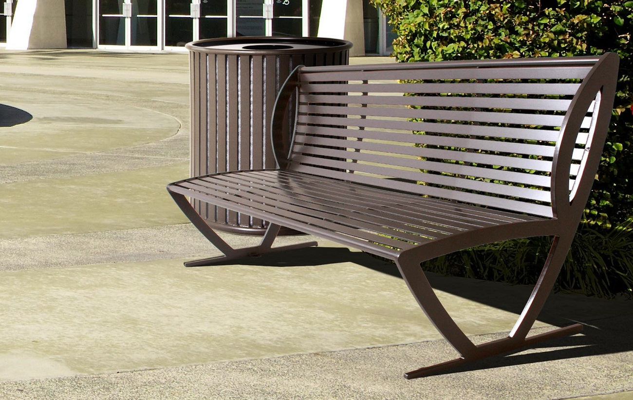 Outdoor metal park bench with backrest and armrests beside matching metal trash receptacle on concrete pavement