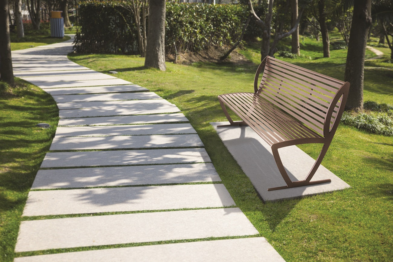 Brown metal outdoor bench with backrest and armrests beside a curved stone pathway in a green park setting