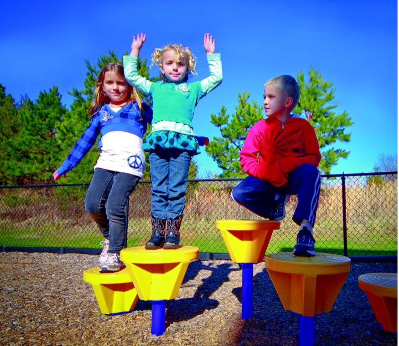 Fun Pods Playground Section, 5 Pods with children balancing on yellow pod tops supported by blue poles in outdoor playground setting