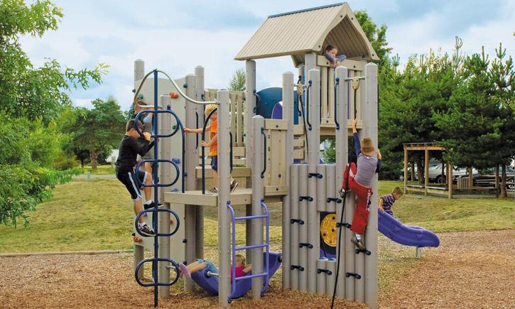 Mountaineer Play System with climbing panels, loop climber, slide, and children playing on beige and purple outdoor structure