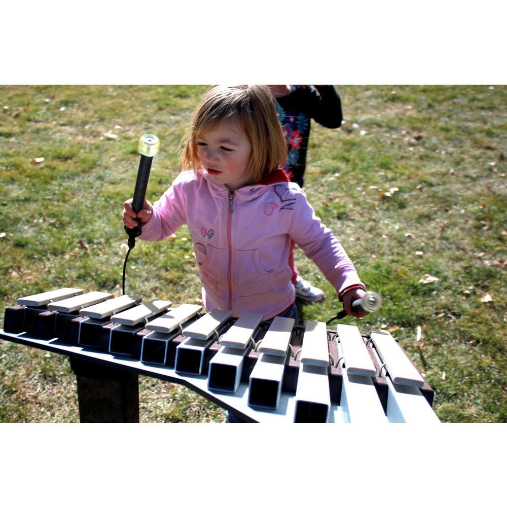 Child playing a brown outdoor musical xylophone with mallets on grass in a park setting