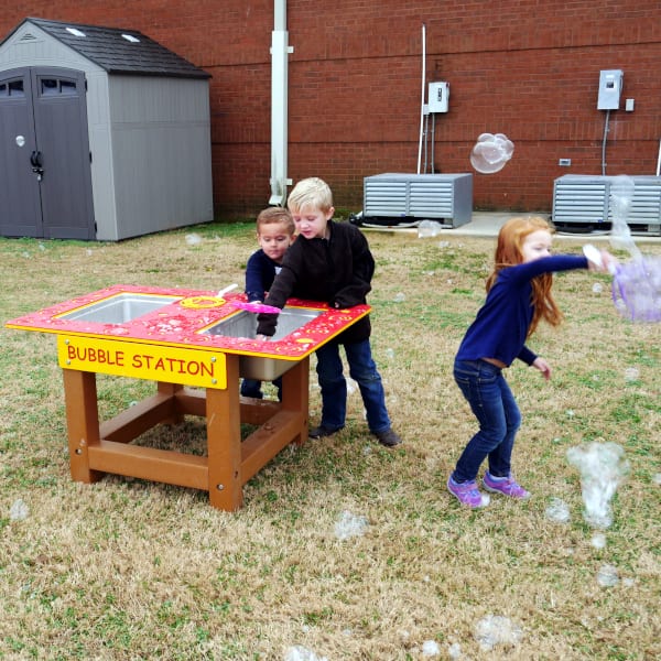 Children playing with an outdoor bubble station, creating bubbles and engaging in sensory, imaginative group play