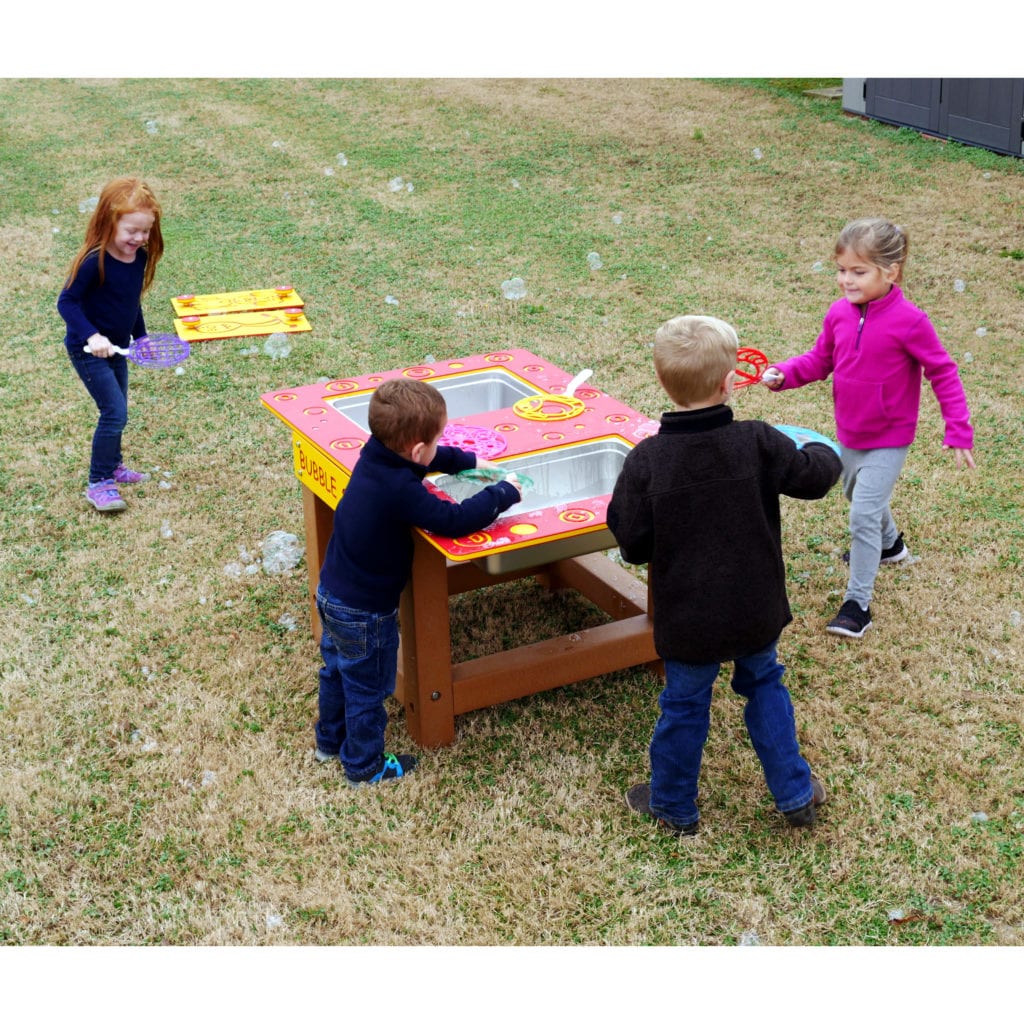 Children playing outdoors with a colorful bubble station featuring bubble wands and soap trays on grass