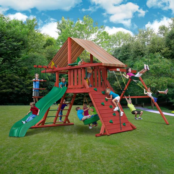 Cedar wooden swing set with multi-color canopy, green slide, rock climbing wall, rope ladder, tire swing, and children playing