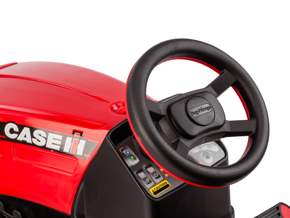Black deluxe steering wheel and dashboard with control buttons and caution label on red pedal ride-on tractor.