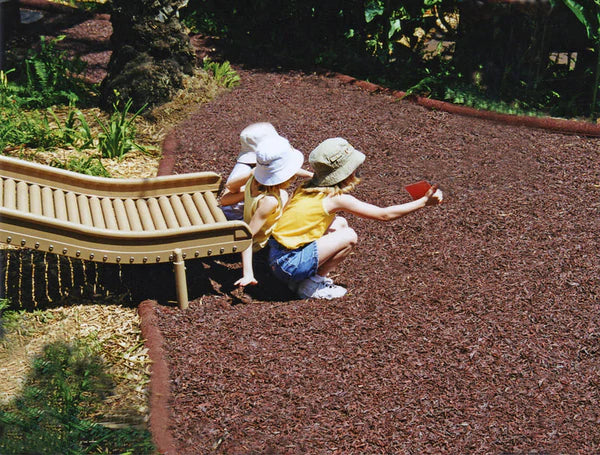 Two children playing on durable, soft loose fill rubber mulch playground surfacing near a slide surrounded by greenery