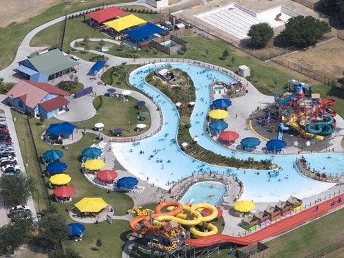 Overhead view of colorful single post umbrella shades in blue, yellow, and red at a waterpark with lazy river and water play structures