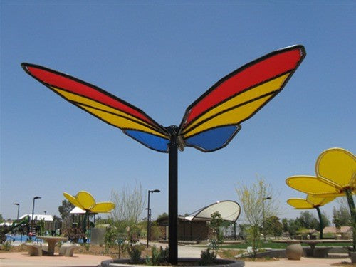 Colorful butterfly wings shade structure with red, yellow, and blue fabric panels in a park setting