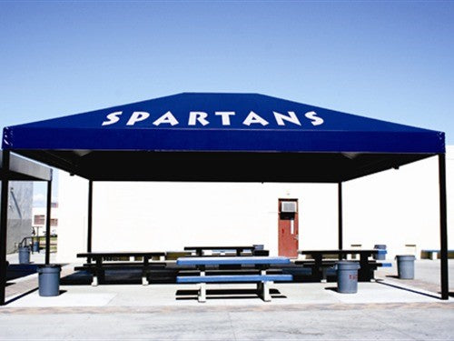 Blue hip roof shade structure with four posts covering picnic tables and trash bins, featuring "Spartans" lettering on canopy