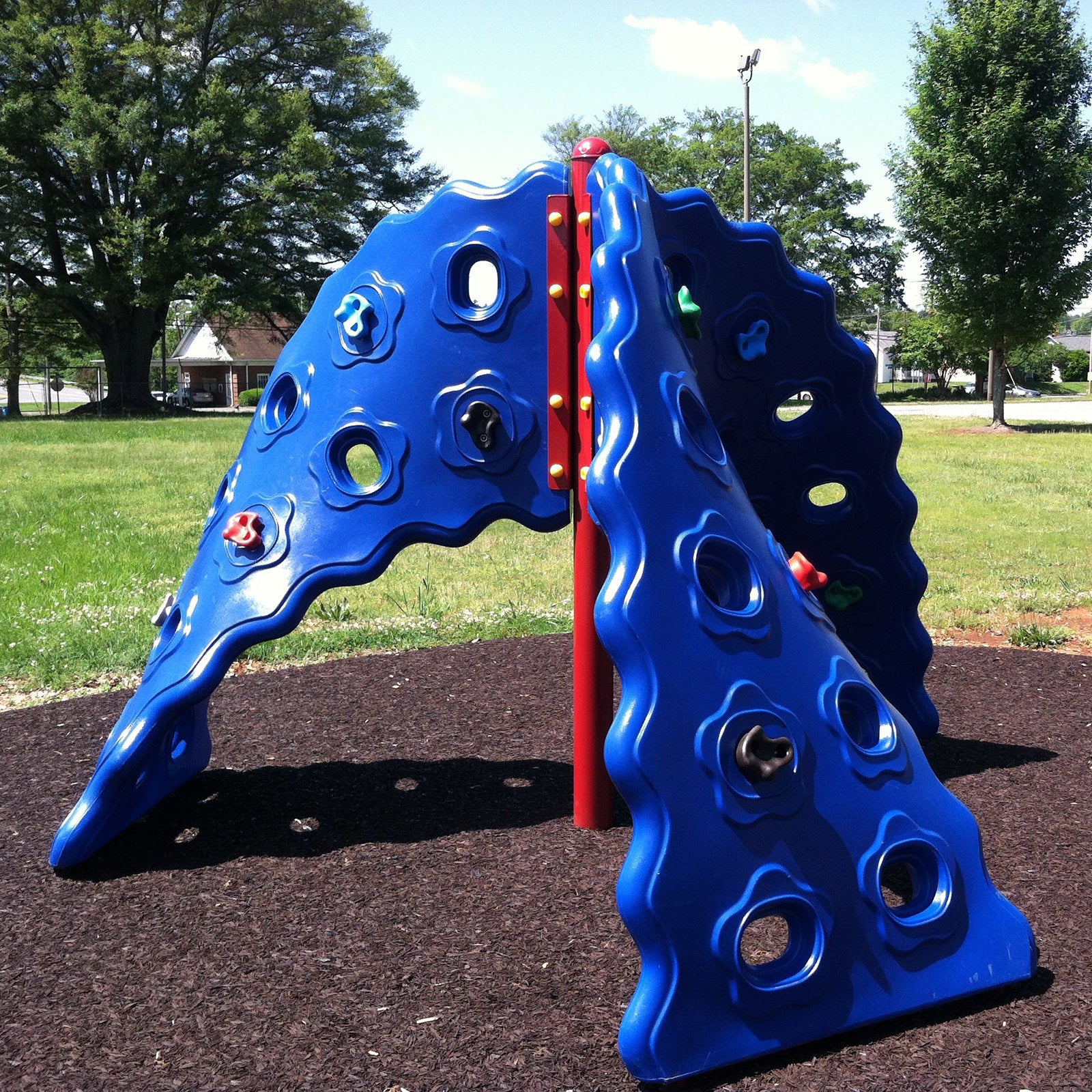Blue curved climbing panels with colorful handholds on red supports in an outdoor playground setting