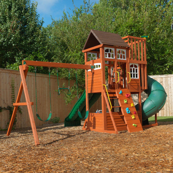 KidKraft Copper Ridge Wooden Swing and Play Set with two belt swings, climbing wall, tube slide, and playhouse deck in backyard.
